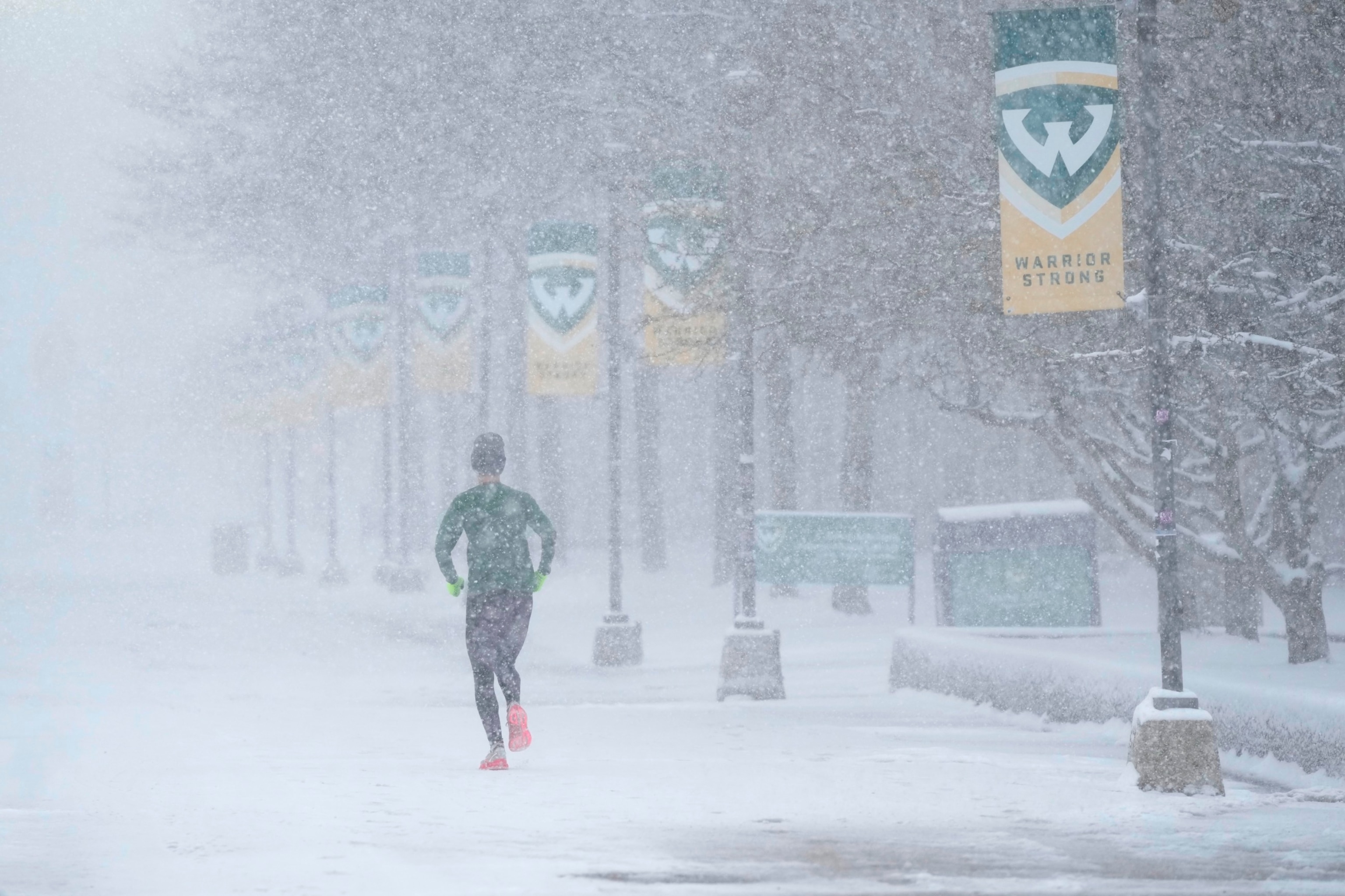 PHOTO: A jogger runs as snow falls on the campus of Wayne State University, March 22, 2024, in Detroit. 