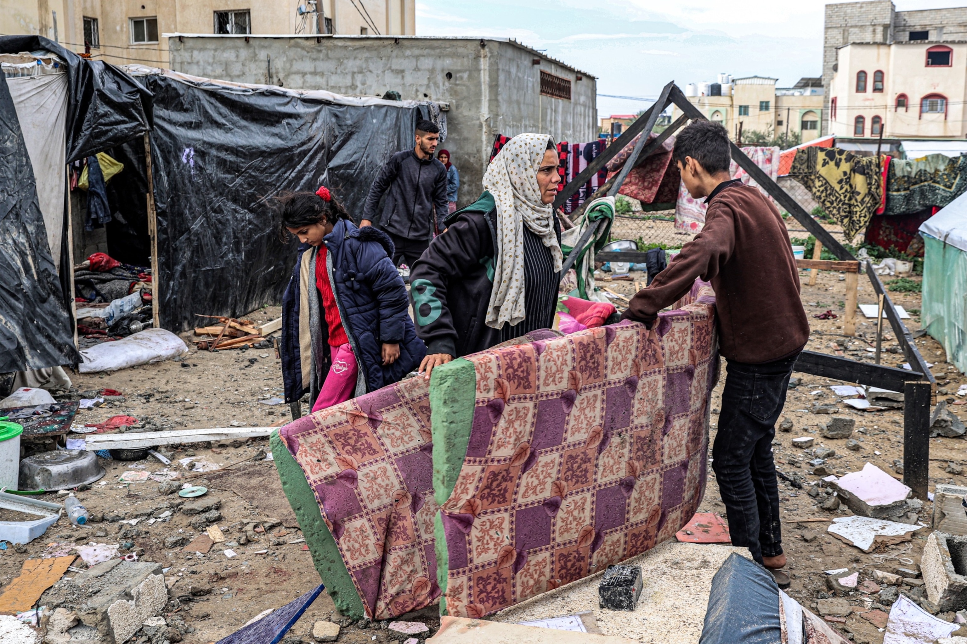PHOTO: A woman and a boy move mattresses while standing before shelters erected outside a damaged building following overnight Israeli bombardment at the Rafah refugee camp in the southern Gaza Strip on March 19, 2024.