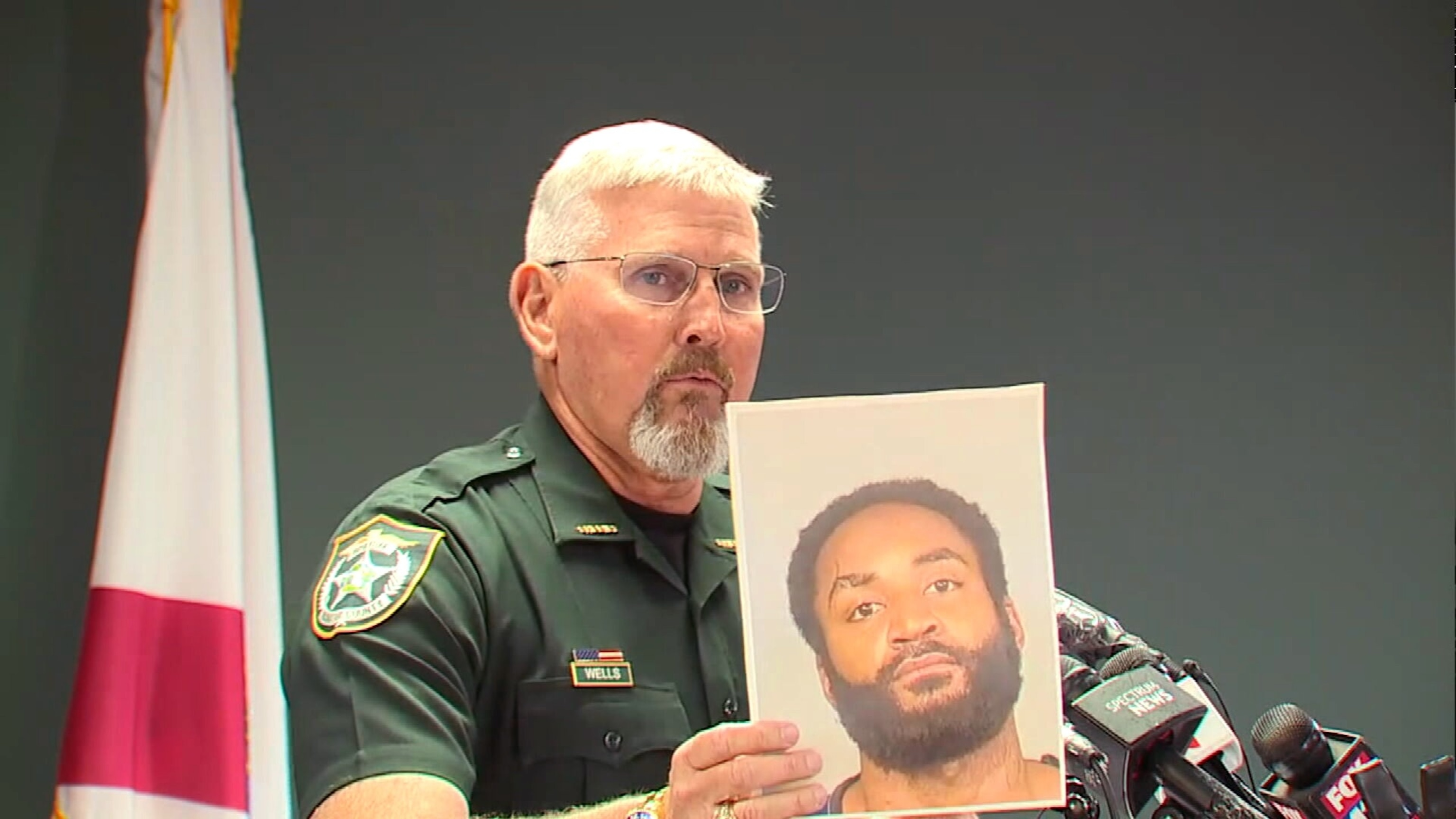 PHOTO: Manatee County Sheriff Rick Wells speaks at a press conference, June 25, 2024, holding a photograph of triple homicide suspect Javontee Brice.