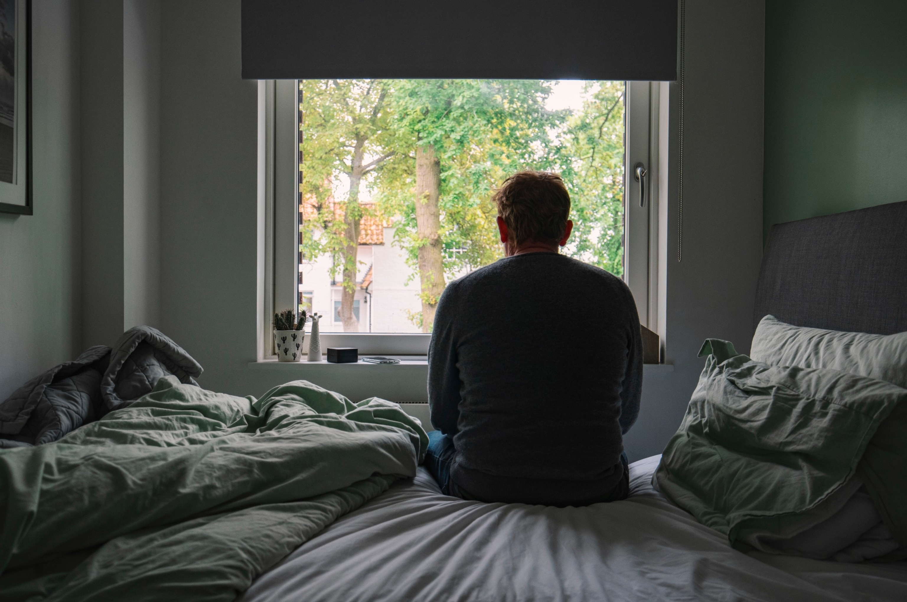 PHOTO: In this undated stock photo, a man is seen sitting alone on his bed as he looks out a window.