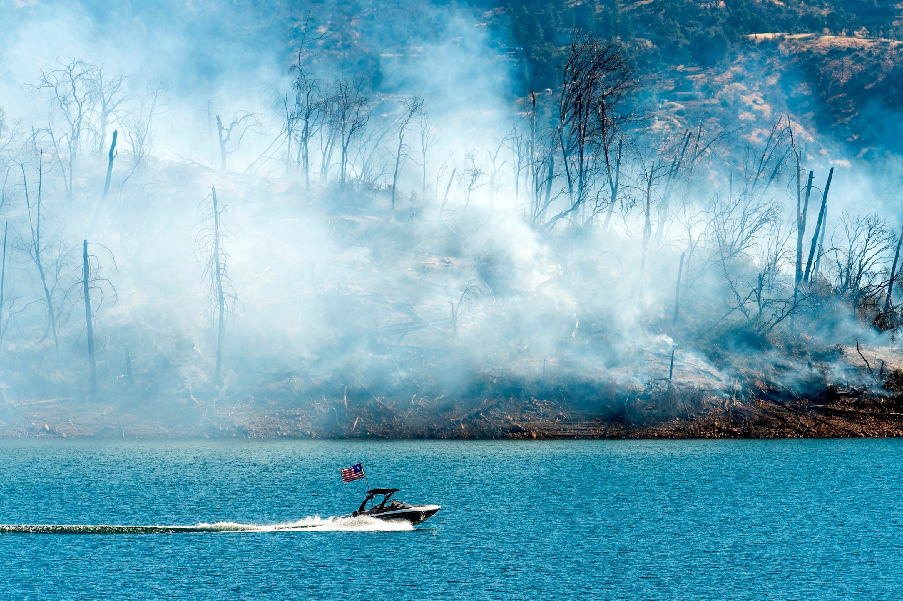 PHOTO: A boat crosses Lake Oroville with a smoldering hillside behind as the Thompson Fire burns in Oroville, Calif., on July 3, 2024.