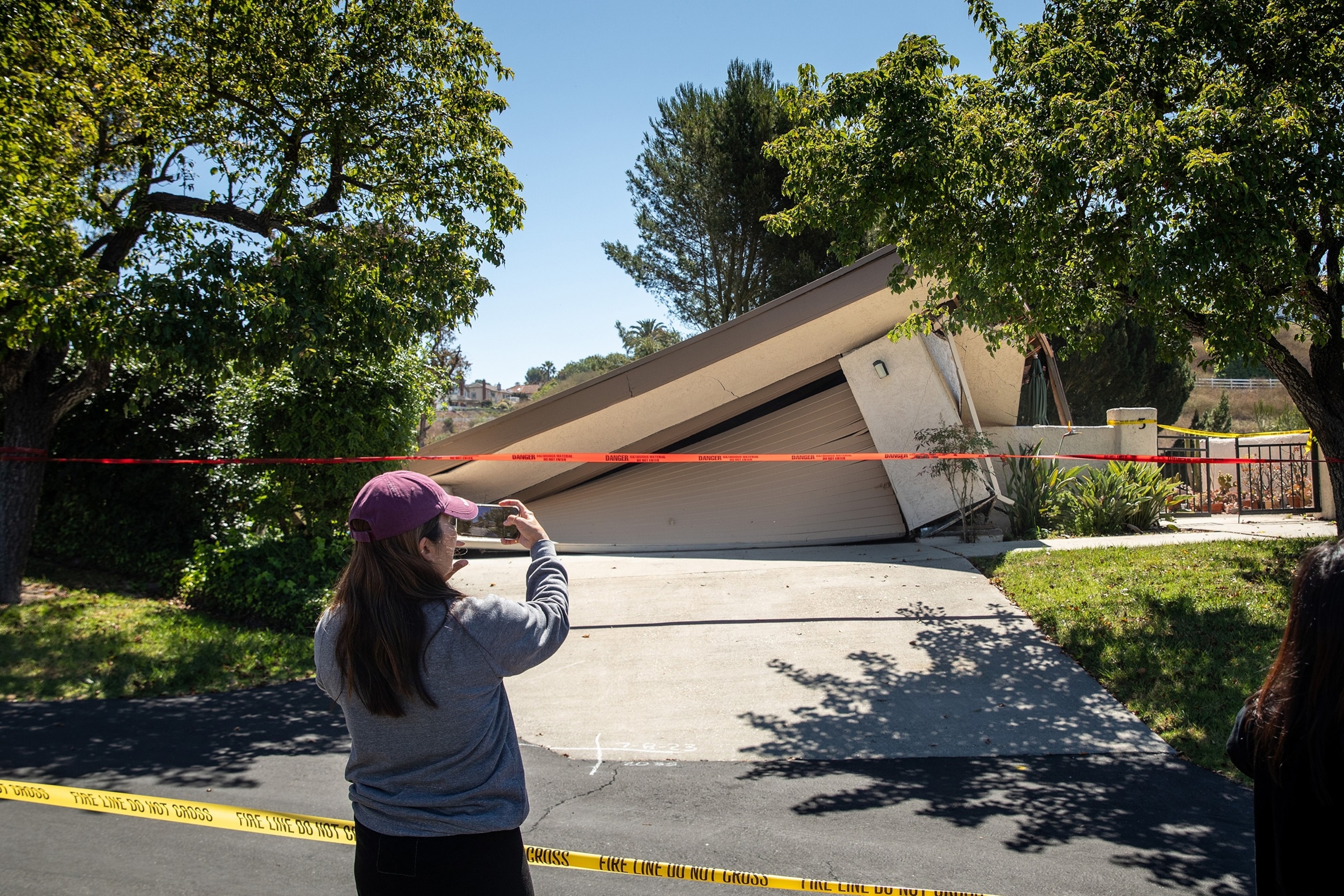 PHOTO: In this July 10, 2023, file photo, a resident of the neighborhood takes a picture of a house with extensive damage along Peartree Ln in Rolling Hills Estates, Calif., the morning after several houses began sliding down a canyon.