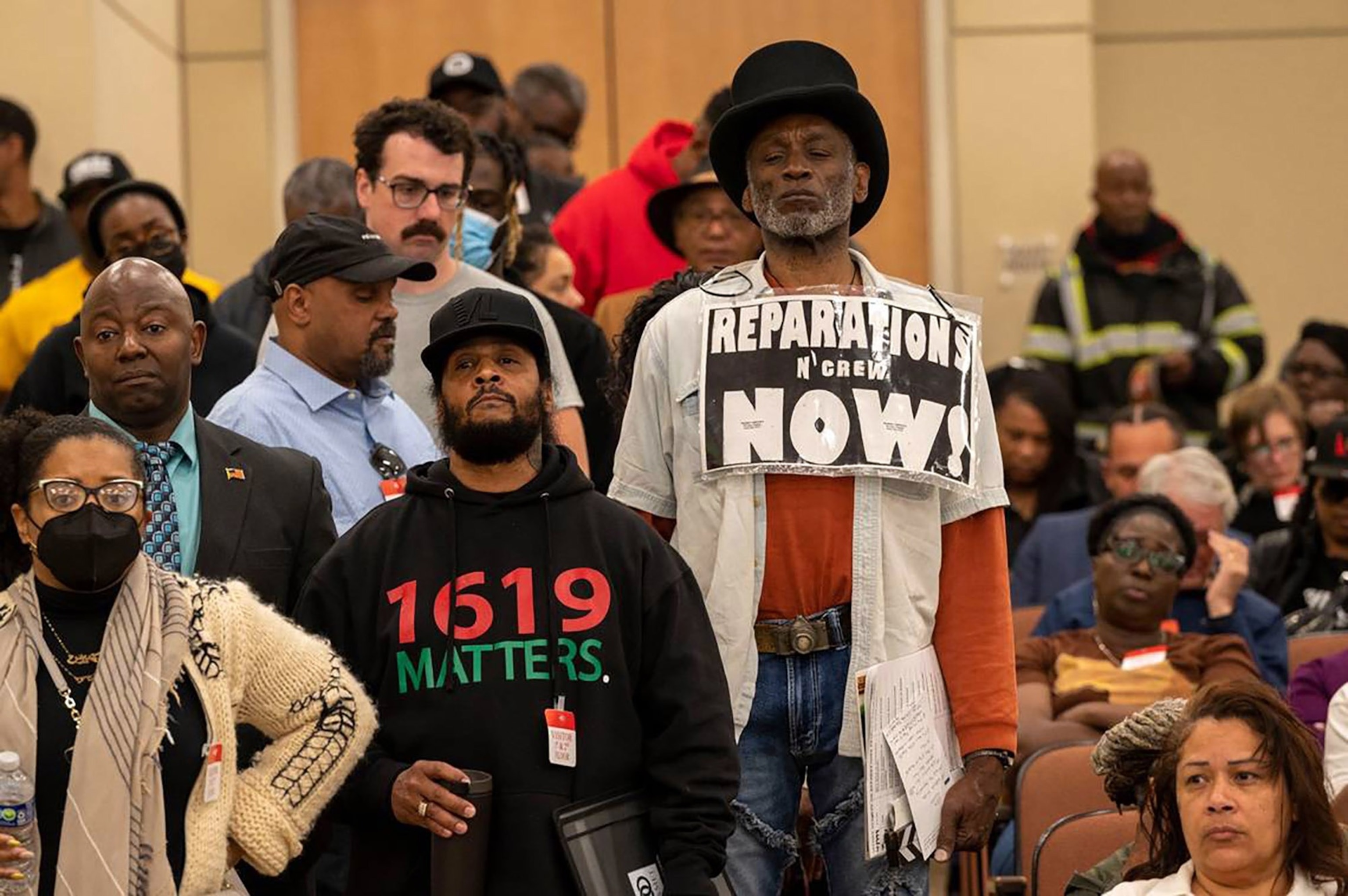 PHOTO: Morris Griffin, wearing a sign that says "reparations now," waits in a line to speak during public comment in 2023 at a meeting of the California Reparations Task Force, at the California Environmental Protection Agency in Sacramento, California.